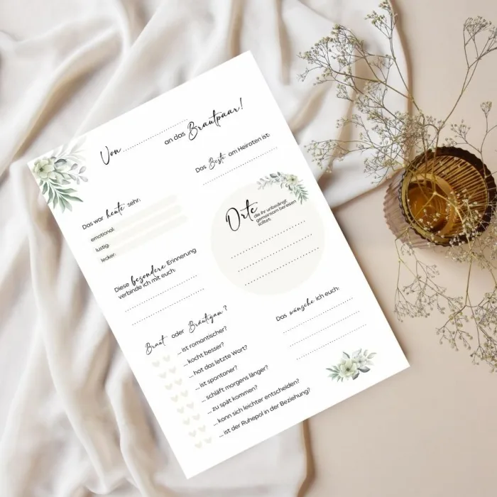Künstlerische Hochzeitseinladung mit Fragebogen auf Tischtuch neben Pflanze