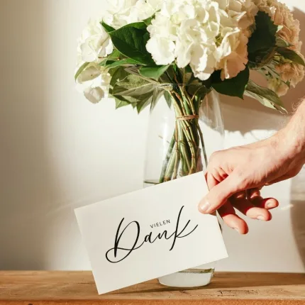 Schlichte Schwarz-Weiß Dankeskarte in einer Hand vor Blumenstrauß - A6 Karte mit 'Danke für deine Bestellung' und Kontaktdaten