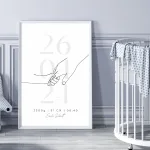 Gerahmtes Geburtserinnerungsbild in grau-schwarz auf dem Boden neben einem Kinderbett – Personalisiert mit Namen, Geburtsdaten und Kinderhand-Motiv