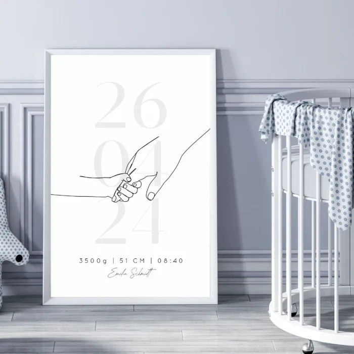 Gerahmtes Geburtserinnerungsbild in grau-schwarz auf dem Boden neben einem Kinderbett – Personalisiert mit Namen, Geburtsdaten und Kinderhand-Motiv