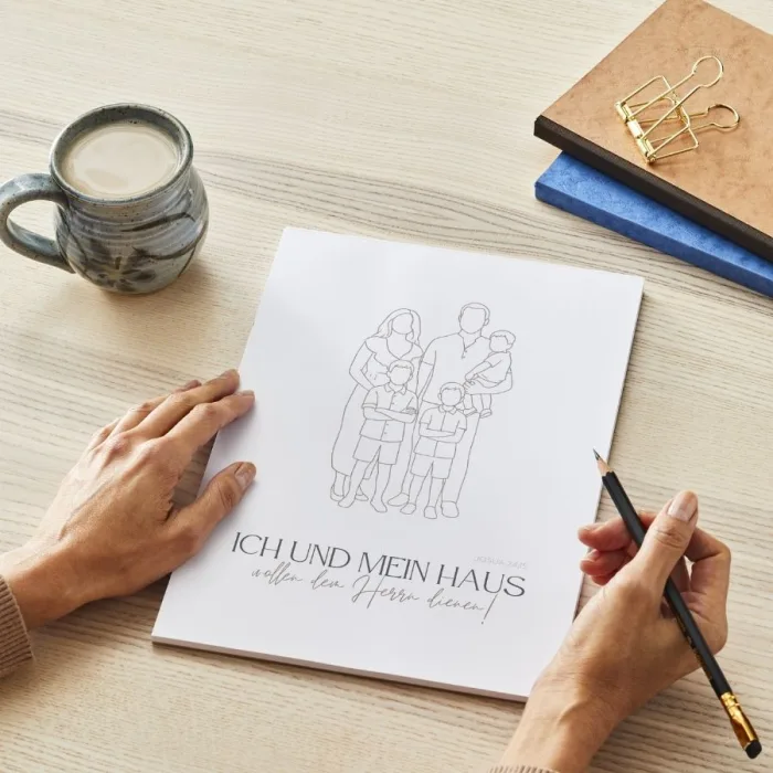 Unerahmtes Familien-Poster im Line-Art Stil mit Bibelvers auf Schreibtisch, daneben Frau mit Bleistift